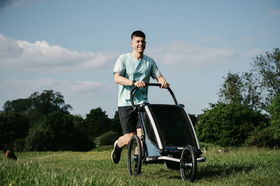 Siôn running across a field pushing a running buggy